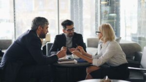 Tre affärspersoner diskuterar vid ett bord i en ljus mötesmiljö